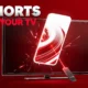 Google TV remote pointing at home screen with vertical YouTube Shorts row replacing movie tiles.